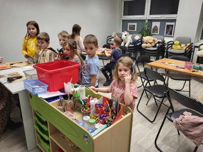 Na zdjęciu znajdują się uczestnicy warsztatów. Dzieci siedzą przy stole i wykonują prace plastyczne. Zdjęcie wykonano w bibliotece.