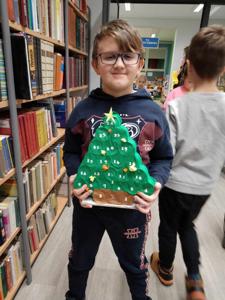 Na zdjęciu znajdują się uczestnicy warsztatów. Dzieci trzymają w rękach choinki. W tle księgozbiór biblioteki. Zdjęcie wykonano w bibliotece.