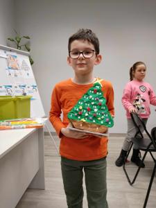 Na zdjęciu znajdują się uczestnicy warsztatów. Dzieci trzymają w rękach choinki. Zdjęcie wykonano w bibliotece.