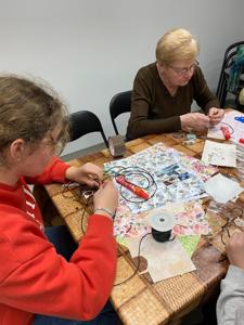 Na zdjęciach znajdują się uczestnicy warsztatów. Uczestnicy siedzą i wykonują rękodzieło.
