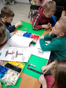 Na zdjęciach znajdują się uczestnicy warsztatów. Uczestnicy siedzą i stoją przy stole. Uczestnicy układają klocki.