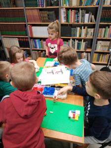 Na zdjęciach znajdują się uczestnicy warsztatów. Uczestnicy siedzą i stoją przy stole. Uczestnicy układają klocki.