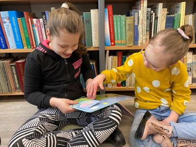 Na zdjęciu znajdują się uczestnicy zajęć. Dzieci siedzą na podłodze. Zdjęcie wykonano w bibliotece. W tle księgozbiór biblioteki.