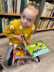Na zdjęciu znajdują się uczestnicy zajęć. Dzieci siedzą na podłodze. Zdjęcie wykonano w bibliotece. W tle księgozbiór biblioteki.