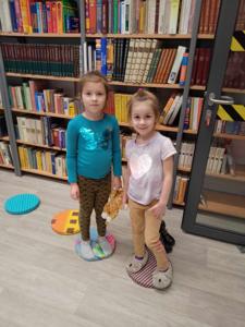 Na zdjęciu znajdują się uczestnicy warsztatów. Uczestnicy stoją. W tle księgozbiór biblioteki.