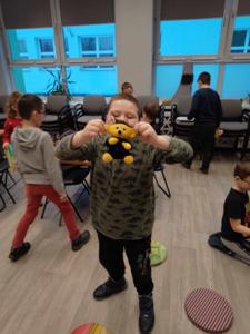 Na zdjęciu znajdują się uczestnicy warsztatów. Uczestnicy stoją. W tle księgozbiór biblioteki.