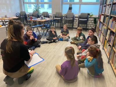Na zdjęciu znajdują się uczestnicy warsztatów. Uczestnicy siedzą. W tle księgozbiór biblioteki.