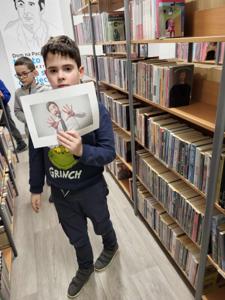 Na zdjęciu znajdują się uczestnicy warsztatów. Uczestnicy stoją. W tle księgozbiór biblioteki.