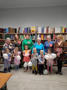 Na zdjęciu znajdują się uczestnicy warsztatów. Uczestnicy stoją. W tle księgozbiór biblioteki.