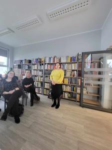 Na zdjęciu znajduje się prelegentka oraz osoby siedzące na krzesłach. W tle wyświetlana prezentacja multimedialna. Zdjęcie wykonano w bibliotece.