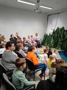 Uczestnicy siedzą na podłodze i na krzesłach. W tle teatrzyk i cienie.