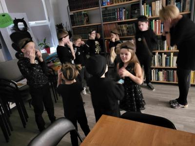 Na zdjęciu znajdują się uczestnicy zajęć. Dzieci stoją i pokazują. różne rzeczy. Zdjęcie wykonano w bibliotece.