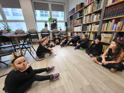 Na zdjęciu znajdują się uczestnicy zajęć siedzący na poduszkach. Zdjęcie wykonano w bibliotece.