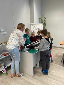 Na zdjęciu znajdują się uczestnicy zajęć. Dzieci patrzą na instrument.