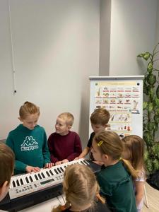 Na zdjęciu znajdują się uczestnicy zajęć. Dzieci patrzą na instrument.