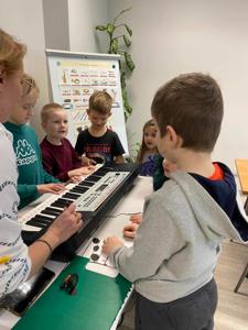 Na zdjęciu znajdują się uczestnicy zajęć. Dzieci patrzą na instrument.