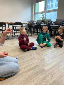 Na zdjęciu znajdują się uczestnicy zajęć. Dzieci siedzą w kręgu na podłodze.