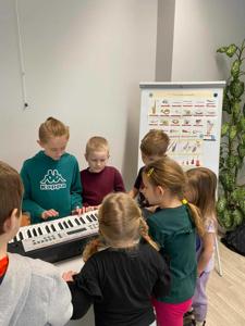Na zdjęciu znajdują się uczestnicy zajęć. Dzieci patrzą na instrument.