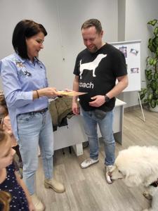 Na zdjęciu zgadują się uczestnicy zajęć. Na zdjęciu znajduje się pies. Kobieta trzyma w rękach kartkę.