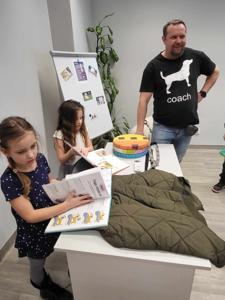 Na zdjęciu zgadują się uczestnicy zajęć. Na zdjęciu znajduje się pies. Uczestnicy stoją i głaskają psa.