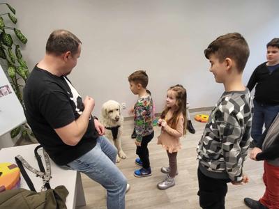 Na zdjęciu zgadują się uczestnicy zajęć. Na zdjęciu znajduje się pies. Uczestnicy stoją i karmią psa.