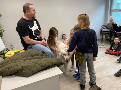 Na zdjęciu zgadują się uczestnicy zajęć. Na zdjęciu znajduje się pies. Uczestnicy stoją i głaskają psa.