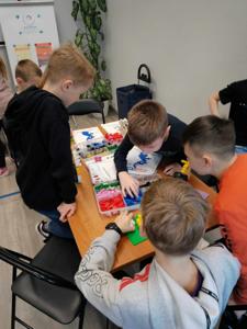 Zdjęcie przestawia uczestników warsztatów lego. Zdjęcie wykonano w bibliotece.