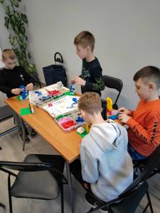 Zdjęcie przestawia uczestników warsztatów lego. Zdjęcie wykonano w bibliotece.