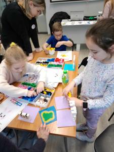 Zdjęcie przestawia uczestników warsztatów lego. Zdjęcie wykonano w bibliotece.