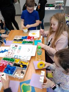 Zdjęcie przestawia uczestników warsztatów lego. Zdjęcie wykonano w bibliotece.
