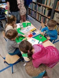 Zdjęcie przestawia uczestników warsztatów lego. Zdjęcie wykonano w bibliotece.