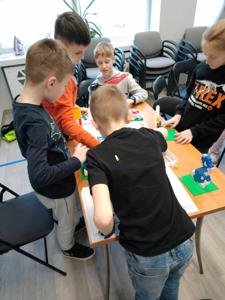 Zdjęcie przestawia uczestników warsztatów lego. Zdjęcie wykonano w bibliotece.