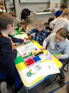 Zdjęcie przestawia uczestników warsztatów lego. Zdjęcie wykonano w bibliotece.