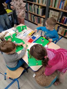 Zdjęcie przestawia uczestników warsztatów lego. Zdjęcie wykonano w bibliotece.