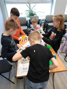 Zdjęcie przestawia uczestników warsztatów lego. Zdjęcie wykonano w bibliotece.