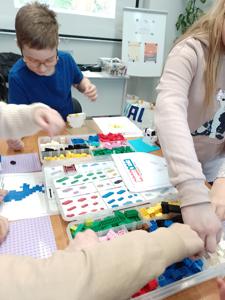 Zdjęcie przestawia uczestników warsztatów lego. Zdjęcie wykonano w bibliotece.