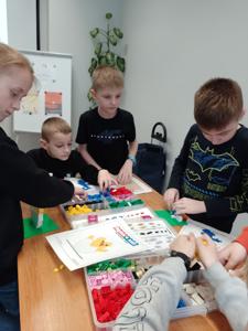 Zdjęcie przestawia uczestników warsztatów lego. Zdjęcie wykonano w bibliotece.