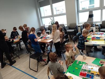 Zdjęcie przestawia uczestników warsztatów lego. Zdjęcie wykonano w bibliotece.