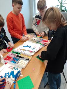 Zdjęcie przestawia uczestników warsztatów lego. Zdjęcie wykonano w bibliotece.