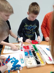Zdjęcie przestawia uczestników warsztatów lego. Zdjęcie wykonano w bibliotece.
