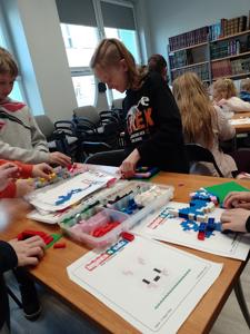 Zdjęcie przestawia uczestników warsztatów lego. Zdjęcie wykonano w bibliotece.