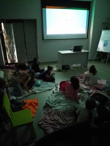Zdjęcie przedstawia uczestników kina w bibliotece. Dzieci oglądają bajkę. Zdjęcie wykonano w bibliotece.