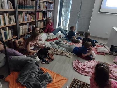 Zdjęcie przedstawia uczestników kina w bibliotece. Dzieci oglądają bajkę. Zdjęcie wykonano w bibliotece.