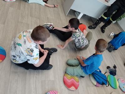 Na zdjęciu znajdują się  dzieci biorące udział w warsztatach pierwszej pomocy. Zdjęcie wykonano w bibliotece.