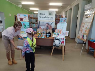 Na zdjęciu znajdują się Dyrektor biblioteki i dziecko nagrodzone w konkursie plastycznym i literackim. Zdjęcie wykonano w  bibliotece.