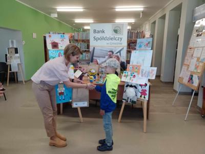 Na zdjęciu znajdują się Dyrektor biblioteki i dziecko nagrodzone w konkursie plastycznym i literackim. Zdjęcie wykonano w  bibliotece.