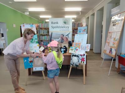 Na zdjęciu znajdują się Dyrektor biblioteki i dziecko nagrodzone w konkursie plastycznym i literackim. Zdjęcie wykonano w  bibliotece.