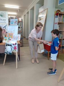 Na zdjęciu znajdują się Dyrektor biblioteki i dziecko nagrodzone w konkursie plastycznym i literackim. Zdjęcie wykonano w  bibliotece.