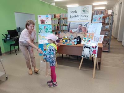 Na zdjęciu znajdują się Dyrektor biblioteki i dziecko nagrodzone w konkursie plastycznym i literackim. Zdjęcie wykonano w  bibliotece.