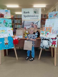 Na zdjęciu znajdują się  dziecko nagrodzone w konkursie plastycznym i literackim. Zdjęcie wykonano w  bibliotece.